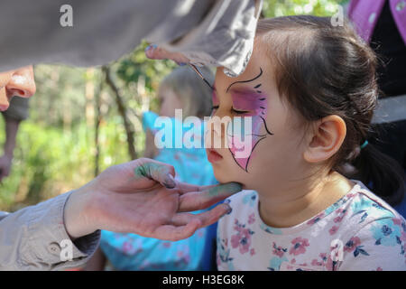 Ragazza carina ottenendo faccia dipinta come una farfalla Foto Stock