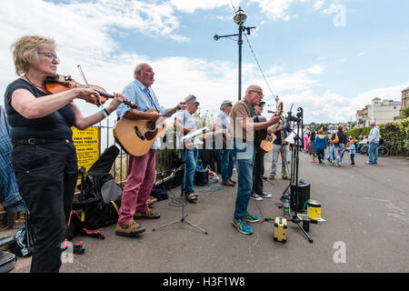 La baia Boys, musicale folk gruppo di alti uomini la riproduzione di chitarre nel sole, insieme con una donna fiddle player, un concerto sul lungomare. Foto Stock