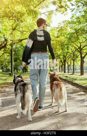 Ragazza giovane con due cani Husky a piedi attraverso il parco Foto Stock