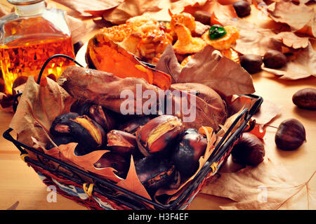 Primo piano di alcune castagne arrostite e patate dolci in una cesta e una piastra con il catalano panellets, e una bottiglia di vetro con sw Foto Stock