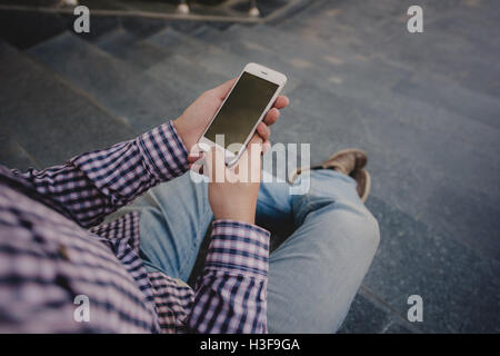 Giovane uomo con il telefono in mano seduti sui gradini. vista superiore Foto Stock