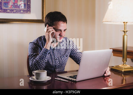 Casualmente vestito giovane imprenditore utilizzando il telefono cellulare e il computer portatile. Foto Stock