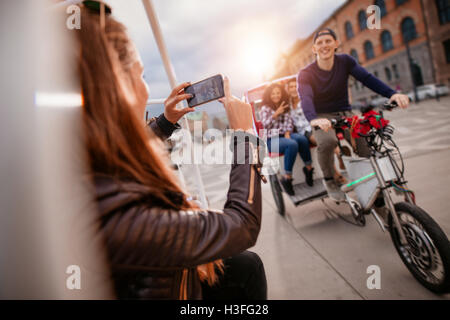 Femmina di scattare fotografie di amici su triciclo ride. Amici godendo le vacanze. Foto Stock