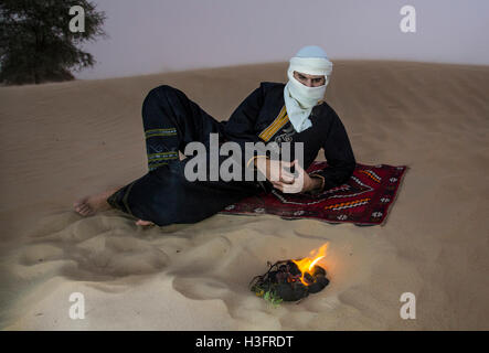 Uomo in tradizionale Tuareg vestito in un deserto, preparando il tè Foto Stock