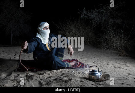 Uomo in tradizionale Tuareg vestito in un deserto, preparando il tè Foto Stock