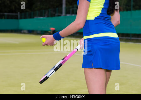 In prossimità di una donna che indossa un abbigliamento sportivo tenendo un tennis bal e una racchetta su un prato verde corte scoperta in primavera o estate Foto Stock