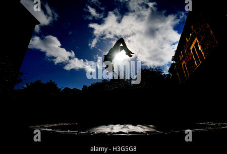 Ragazzo in silhouette, capovolto mentre trampolining in un giardino urbano contro un sole luminoso. *Può essere modello rilasciato su richiesta di Foto Stock