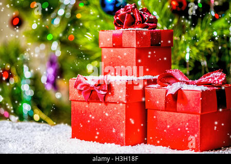 Concetto di vacanza di Natale di rosso confezioni regalo con fiocco su sfondo di legno e neve su albero di Natale decorato, close up Foto Stock