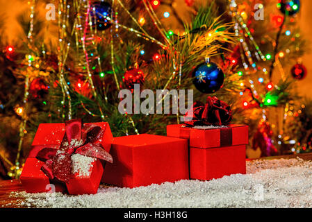 Concetto Nuovo anno di vacanza di aperto rosso confezioni regalo su sfondo di legno e neve su albero di Natale decorato, close up Foto Stock