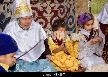 Nonne e bambini battendo la lana in filato accanto yurta presso il villaggio degli Unni Kazakistan Foto Stock