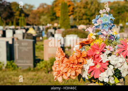 Fiori in un cimitero con lapidi in background al tramonto Foto Stock