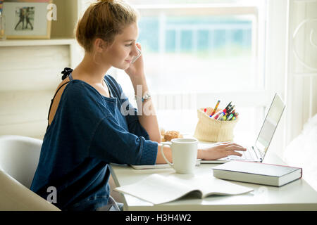 Donna felice utilizzando app Telefono in accogliente casa-ufficio Foto Stock