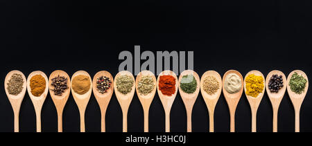 Varie spezie in cucchiai di legno su sfondo nero. Vista dall'alto. Foto Stock