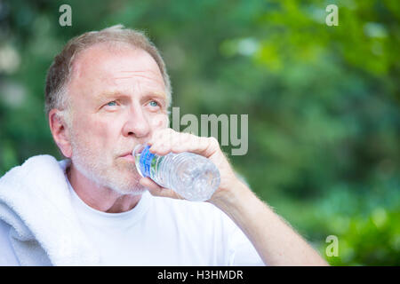 Closeup ritratto, sete senior uomo maturo acqua potabile al di fuori, isolato albero verde sullo sfondo del fogliame Foto Stock