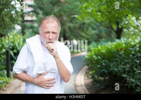 Closeup ritratto, vecchio gentleman in camicia bianca con asciugamano, tosse e tenendo lo stomaco, isolati alberi e arbusti verdi Foto Stock