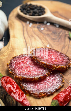 Salame essiccato in crosta nella massa di peperone rosso su sfondo scuro Foto Stock