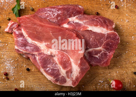Carne di maiale cruda bistecche sulla tavola di legno con erbe aromatiche Foto Stock