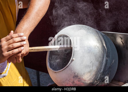 L'uomo la preparazione di olio di semi di girasole rivestito di caramello con un lungo cucchiaio di legno in una pentola rotatorio Foto Stock