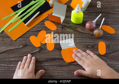 Il bambino crea un messaggio di saluto di imballaggio per lecca-lecca sulla zucca di Halloween carta, essere incollato per la carta i dettagli. Bambini arte pr Foto Stock