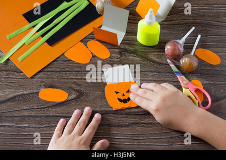 Il bambino crea un messaggio di saluto di imballaggio per lecca-lecca sulla zucca di Halloween carta, essere incollato per la carta i dettagli. Bambini arte pr Foto Stock