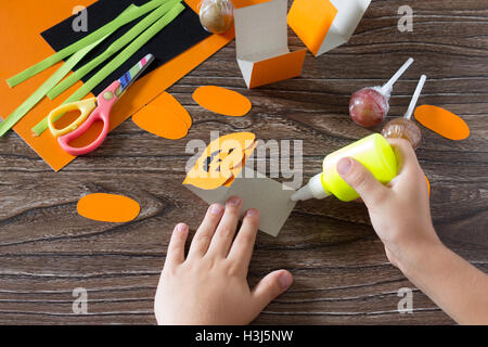 Il bambino crea un messaggio di saluto di imballaggio per lecca-lecca sulla zucca di Halloween carta, essere incollato per la carta i dettagli. Bambini arte pr Foto Stock