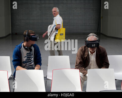 Due uomini che indossano occhiali VR in noiose e ambiente sterile, con il terzo uomo passando a guardarli. Colonia, Germania Foto Stock