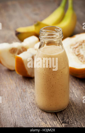 Melone frullato di banana in una bottiglia di vetro, fette di melone, banana sul vecchio sfondo di legno Foto Stock