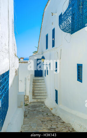 La stretta stradina con un luminoso cielo blu e la stretta striscia di mare sullo sfondo, Sidi Bou Said, Tunisia. Foto Stock