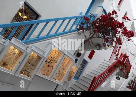 Una stretta strada ondulata di Mykonos con un negozio per la presentazione di articoli di gioielleria contro uno sfondo di rosso bouganville Foto Stock