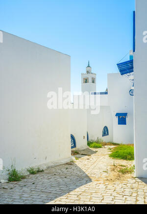 La strada stretta con il cottage bianco conduce alla moschea locale con un alto minareto, Sidi Bou Said, Tunisia. Foto Stock