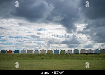 Un drammatico cielo pieno di nuvole sopra Cabine sulla spiaggia, sul lungomare a Lancing verde, a Lancing, West Sussex, in Inghilterra. Foto Stock