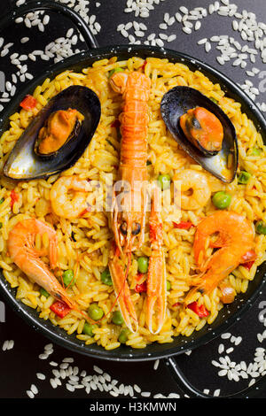 La paella spagnola su sfondo nero con riso intorno al pan Foto Stock