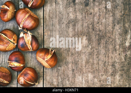 Arrosto di castagne su grigio tavola in legno rustico. Vista da sopra con abbondanza di spazio di copia Foto Stock