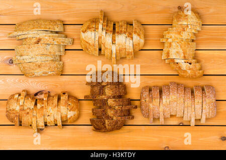 Vista dall'alto in basso su sei fette di pani di varie grano e farina bianca pane in formazione sfalsata su sfondo di legno Foto Stock