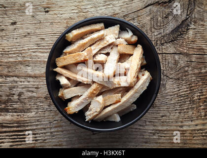 Ciotola nero di carne di maiale alla griglia le fette su un tavolo di legno, vista dall'alto Foto Stock