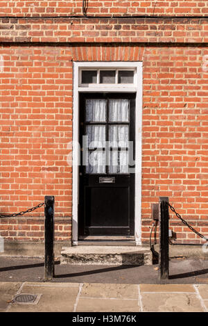 Vittoriano esterno nero porta in legno con pannelli di vetro su un rosso classico muro di mattoni Foto Stock