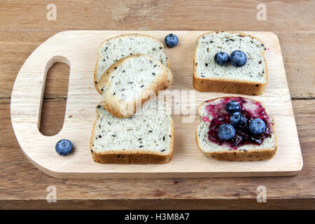 Vegetariano sesamo nero pane topping mirtillo marmellata di ribes e mirtilli freschi sulla tavola di legno Foto Stock