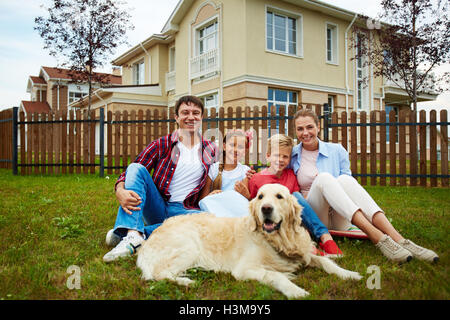 Famiglia di nuovi coloni seduta sul prato con la loro casa dietro Foto Stock
