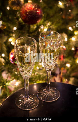 Un set di due flauti champagne riempito con champagne in appoggio su un tavolo di fronte a un albero di Natale. Foto Stock