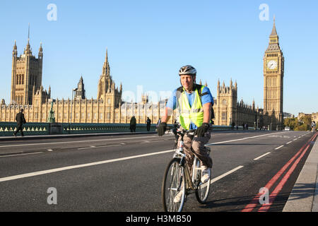 Ciclista viaggia lungo il percorso in bicicletta sul Westminster Bridge, con le case del Parlamento e il Big Ben in background. Mattina di sole in oc Foto Stock