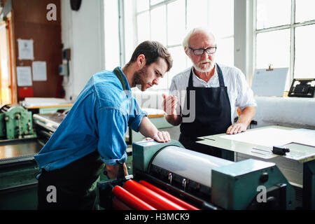 Senior artigiano/tecnico di inquadramento dei giovani uomo sulla macchina di stampa in rilievo nel libro OFFICINA DELLE ARTI Foto Stock