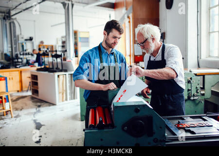 Senior artigiano/tecnico di inquadramento dei giovani uomo sulla macchina di stampa in rilievo nel libro OFFICINA DELLE ARTI Foto Stock