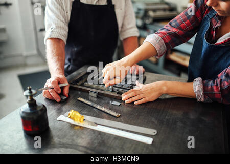 Senior artigiano lavorando su stampa tipografica con giovani craftswoman nel laboratorio di stampa, metà sezione Foto Stock