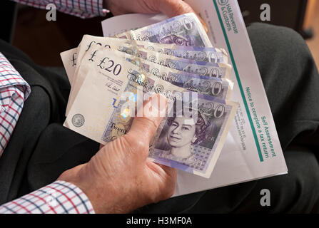 Primo piano di persona uomo in possesso di banconote da venti sterline inglesi in denaro contante banconote e ritorno fiscale di autovalutazione Inghilterra Regno Unito Gran Bretagna Foto Stock