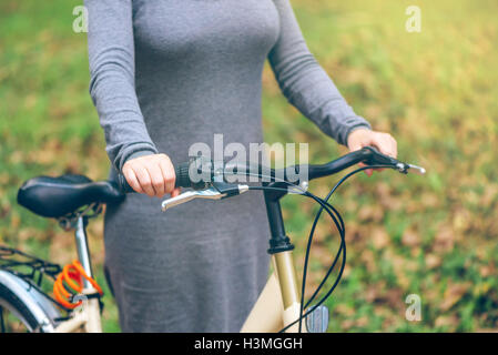 La donna pone con la sua bicicletta nel parco durante l'autunno. Irriconoscibile attraente giovane femmina adulta con vintage retrò bike Foto Stock