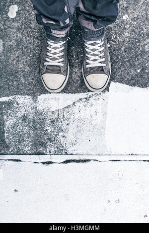 Giovane uomo adulto che indossa sneakers permanente sulla strada, vista da sopra sulle sue gambe e piedi Foto Stock