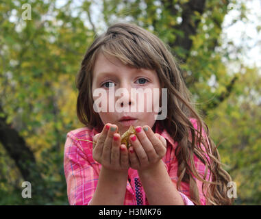 Giovani dai capelli lunghi ragazza con colorati plaid shirt holding cadono le foglie e li di soffiaggio in caduta aria Foto Stock