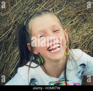 Giovane ragazza bionda sorridente scherzosamente durante la riproduzione sulla balla di fieno Foto Stock