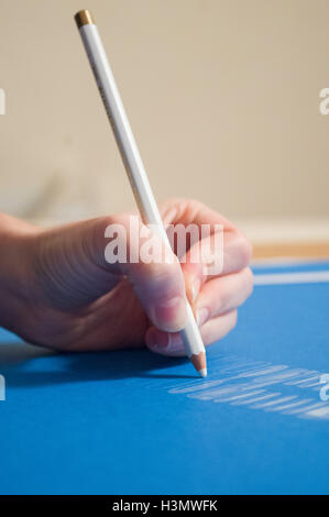 A sinistra del disegno a mano utilizzando una matita bianca su carta blu Foto Stock