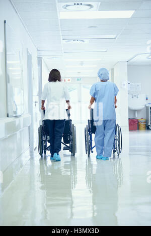 Vista posteriore del orderlies femmina spingendo carrozzine lungo il corridoio di ospedale Foto Stock